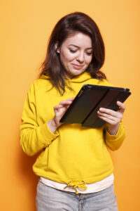 Close-up of caucasian woman utilizing tablet with a touch screen. Smiling female individual holding digital device and looking at screen, working on online related projects.